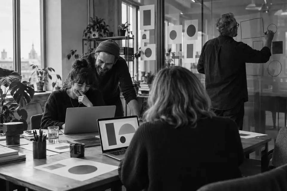 Illustration: a team trying something new on two laptops while a colleague sketches on a glass wall